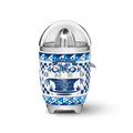 Smeg Dolce & Gabbana Blu Mediterraneo citrus juicer with stainless steel body and vibrant blue design, displayed on a kitchen countertop.