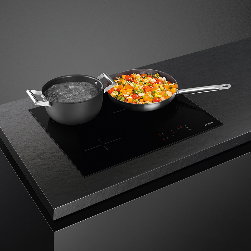 Smeg 60cm ceramic hob with four cooking zones, sleek black surface, and control knobs, installed in modern kitchen setting.